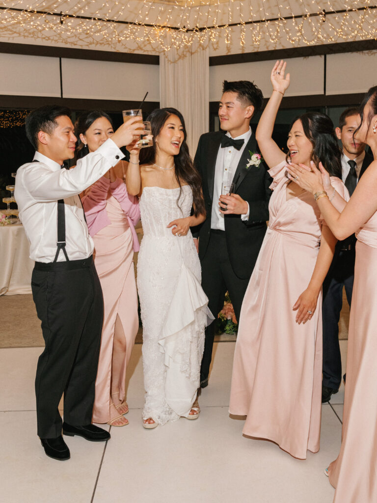 Candid bride and groom reception entrance celebration with pink bridesmaid dresses and cocktail toasts