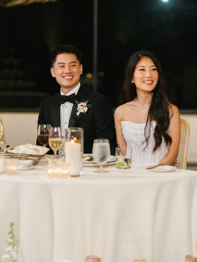 Bride and groom smiling at the sweetheart table during wedding reception toasts at their indoor reception