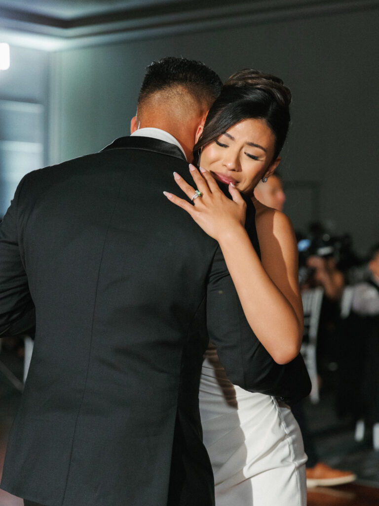 Close up look at an emotional bride holding her husband and showing her engagement ring during the wedding first dance