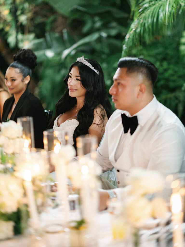Newlyweds looking at the speaker during wedding reception toasts at an outdoor garden reception dinner