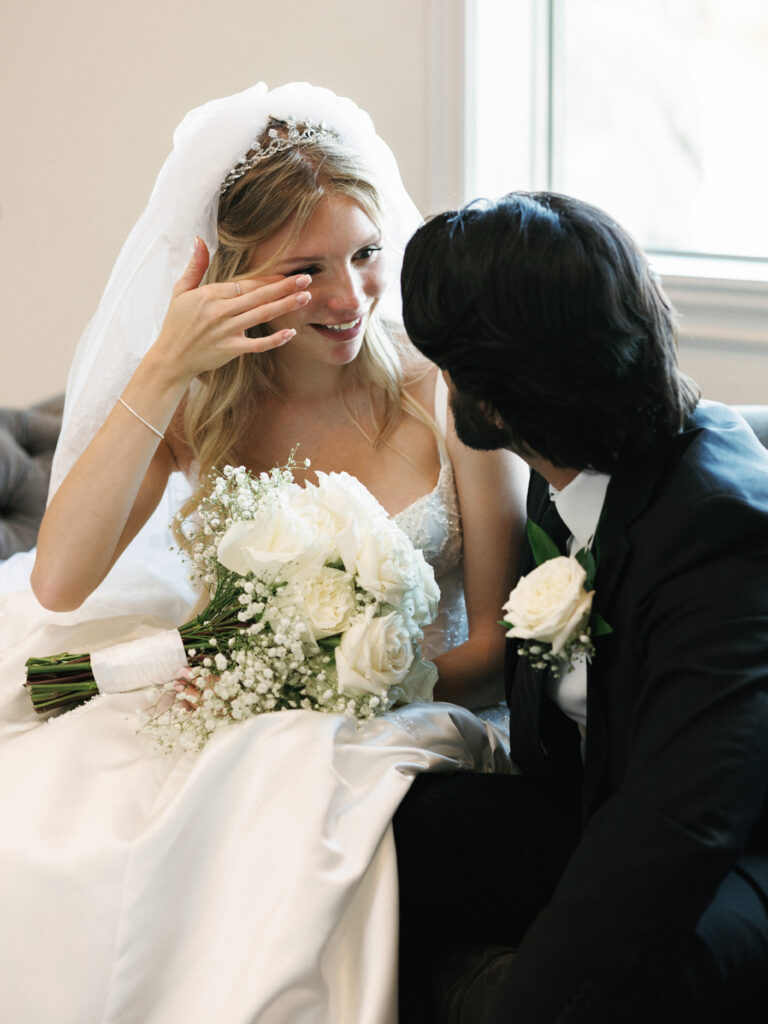 Emotional wedding photography showing a touched bride with a white bouquet sitting with her husband