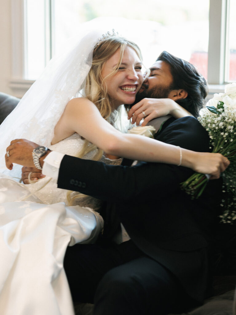 Candid wedding photography capturing a joyful bride laughing while embracing her groom on a couch