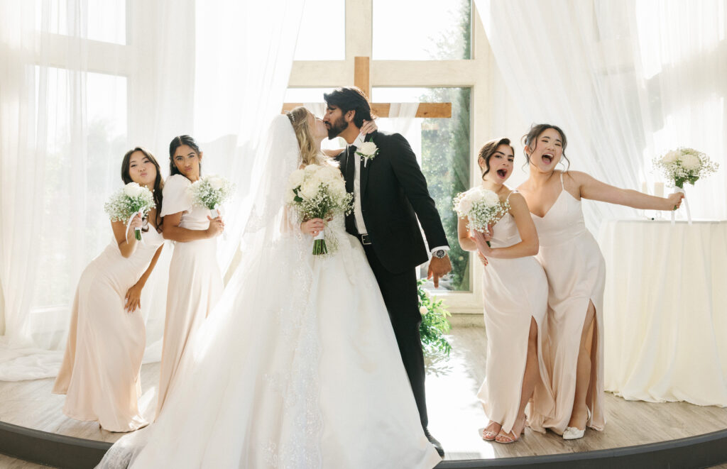 Bridesmaids in elegant champagne satin dresses posing playfully with bouquets during an indoor luxury wedding ceremony