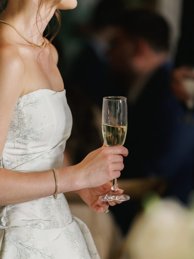 Bride holding a champagne glass while listening to wedding reception toasts from her guests