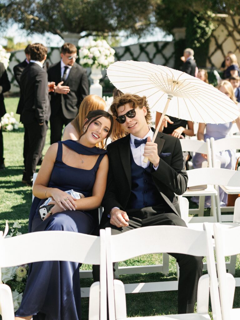 Wedding guests holding a paper parasol to stay in the shade during a ceremony highlighting texas summer wedding tips