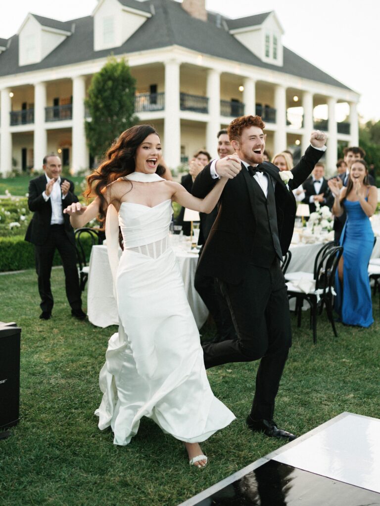 Newlyweds running and laughing during their luxury estate wedding reception entrance outdoor