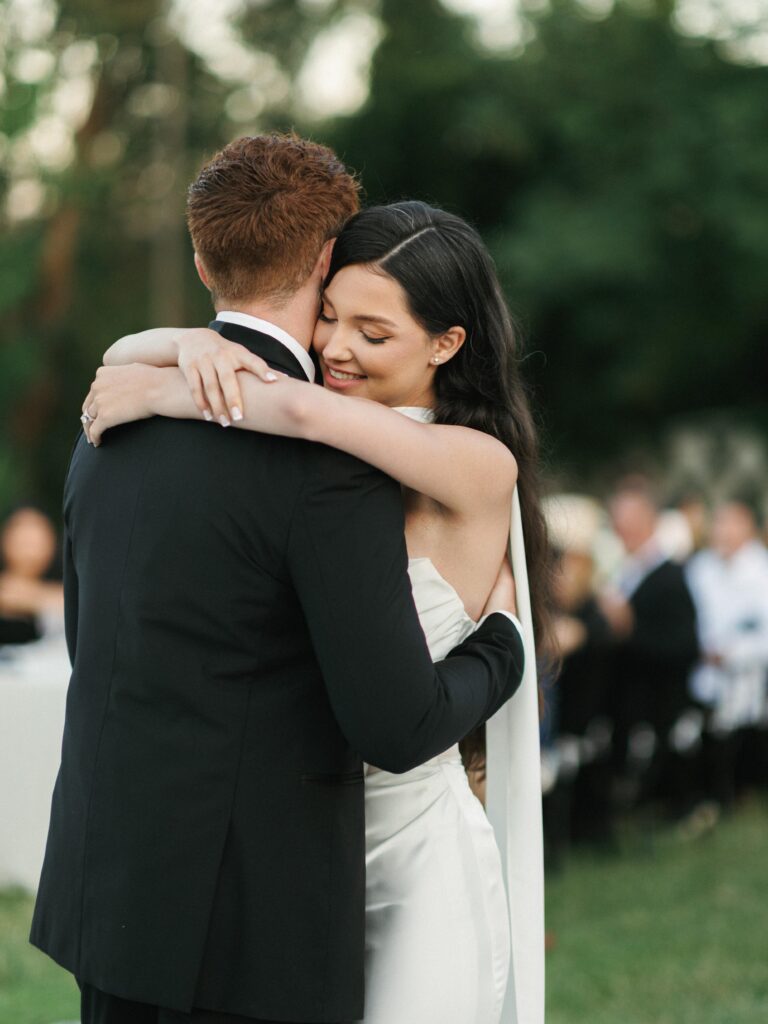 Romantic bride hugging her groom neck during an outdoor wedding first dance surrounded by nature