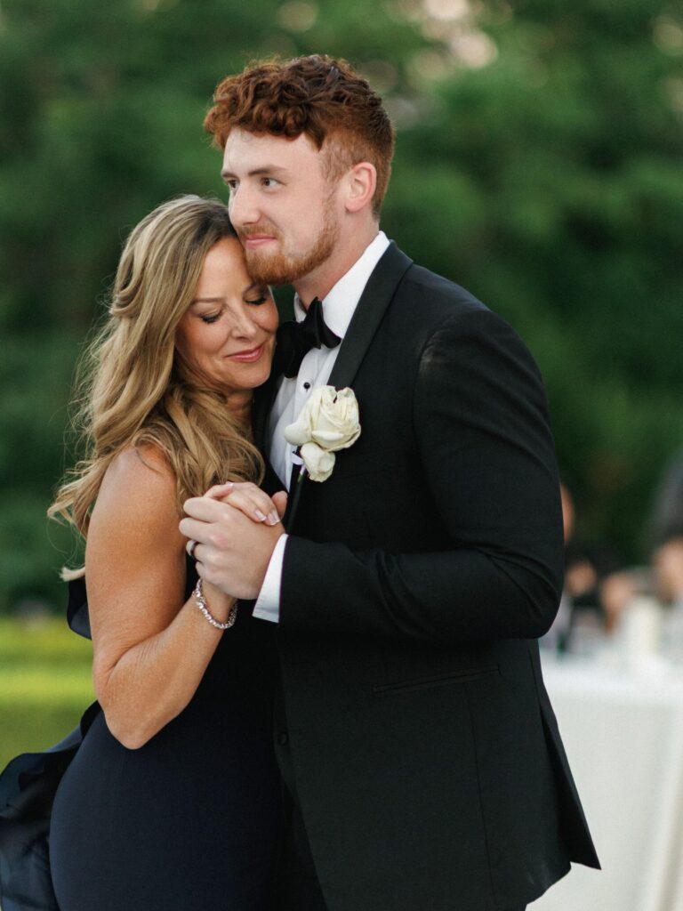 Mother of the groom in a navy blue dress smiling during a romantic mother son dance moment