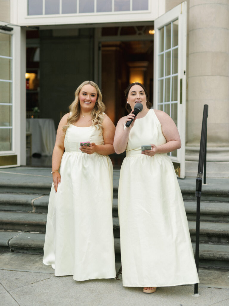 Bridesmaids in elegant ivory dresses holding a microphone and smartphone to give wedding reception toasts