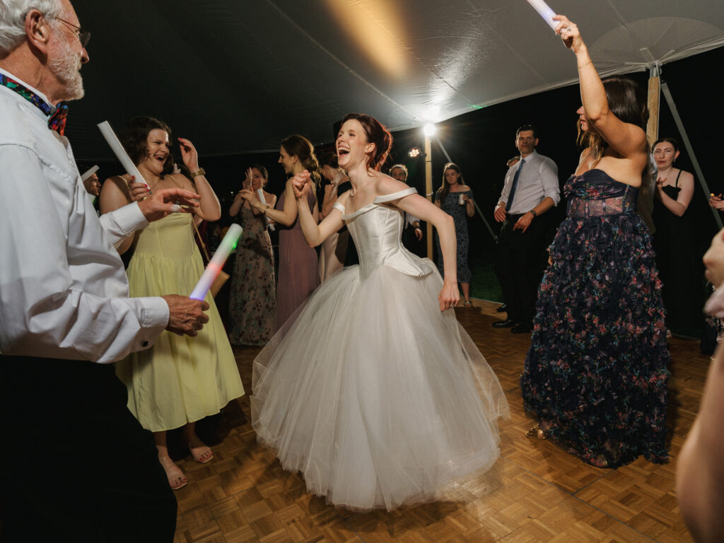 Energetic wedding after party dancing moments with glow sticks and open air tent lighting