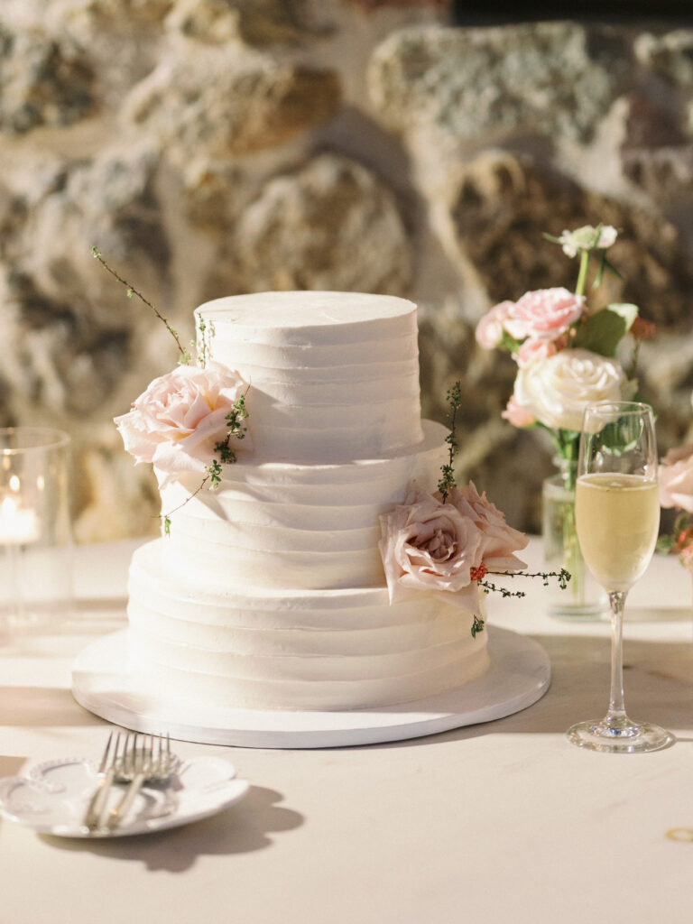 Elegant textured wedding cake with blush roses near a champagne glass and floral arrangement
