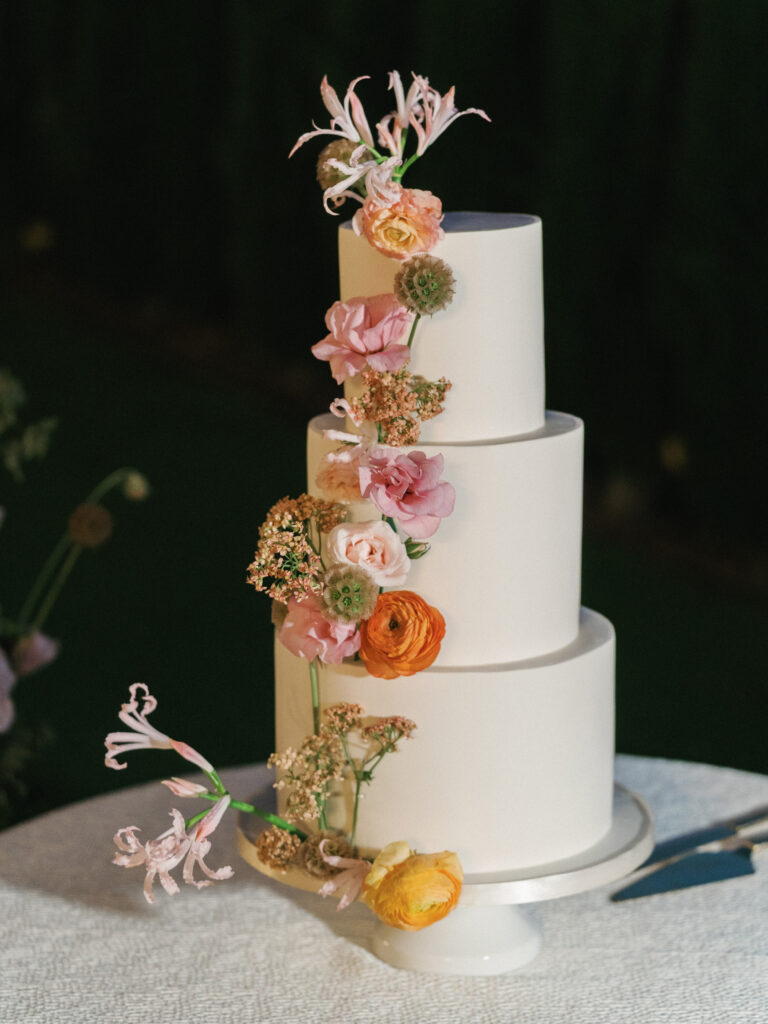 Modern three tier wedding cake decorated with cascading colorful summer garden flowers