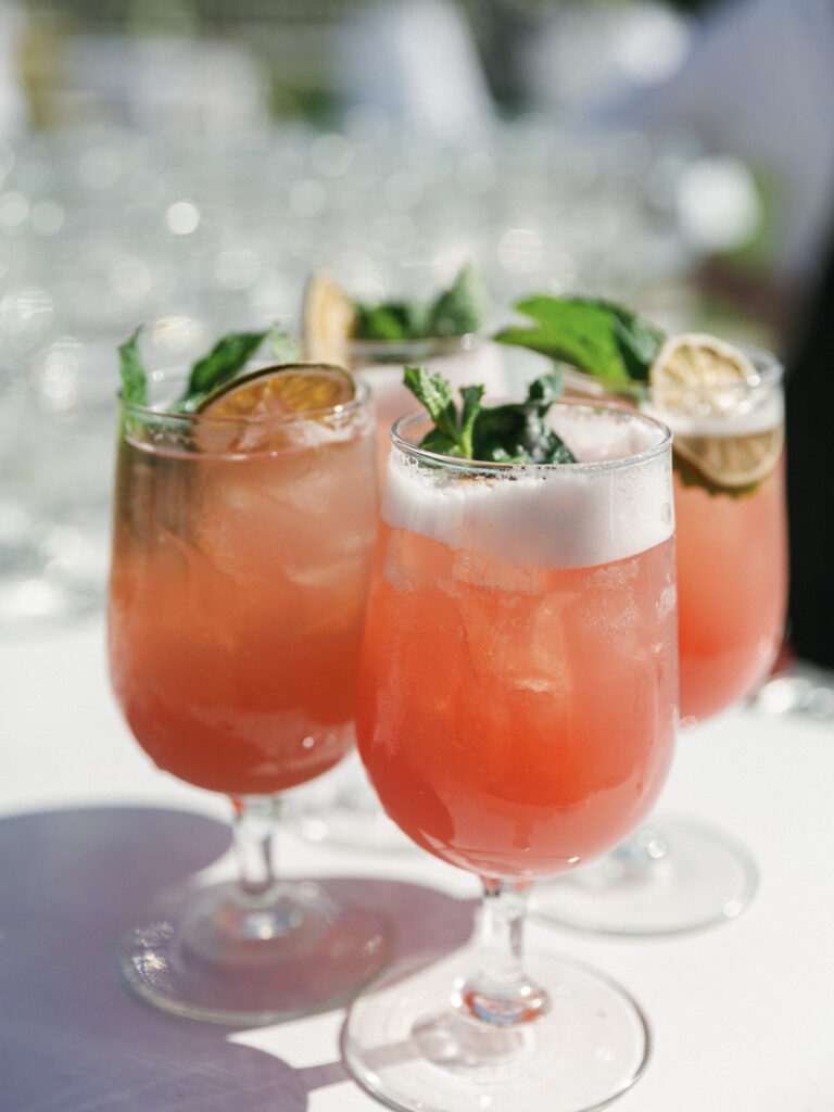 Pink wedding cocktails inside clear glasses displayed on a bar table for an upscale outdoor cocktail hour inspiration