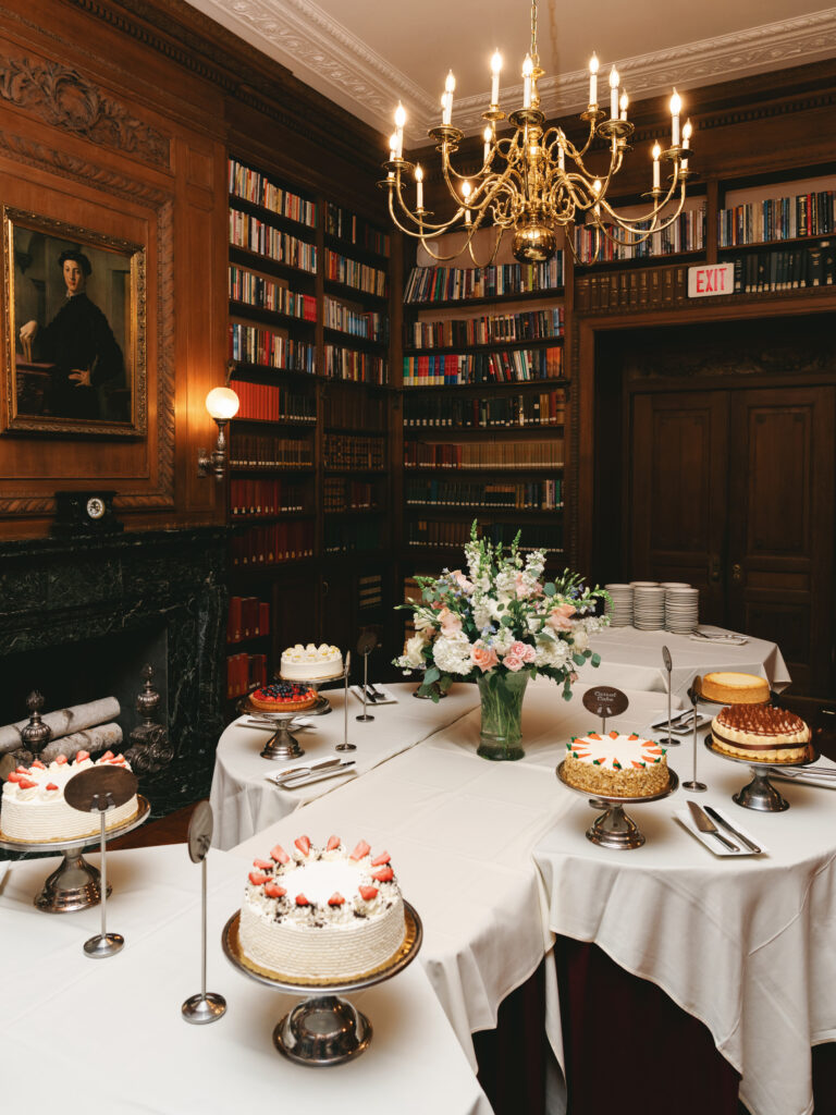 Grand library room wedding reception dessert display with classic wooden bookshelves and fine confections