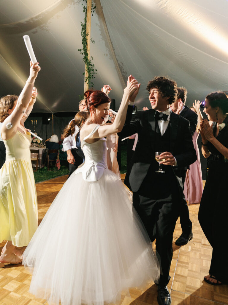 Bride and groom dancing under a wedding tent with guests holding light up foam sticks