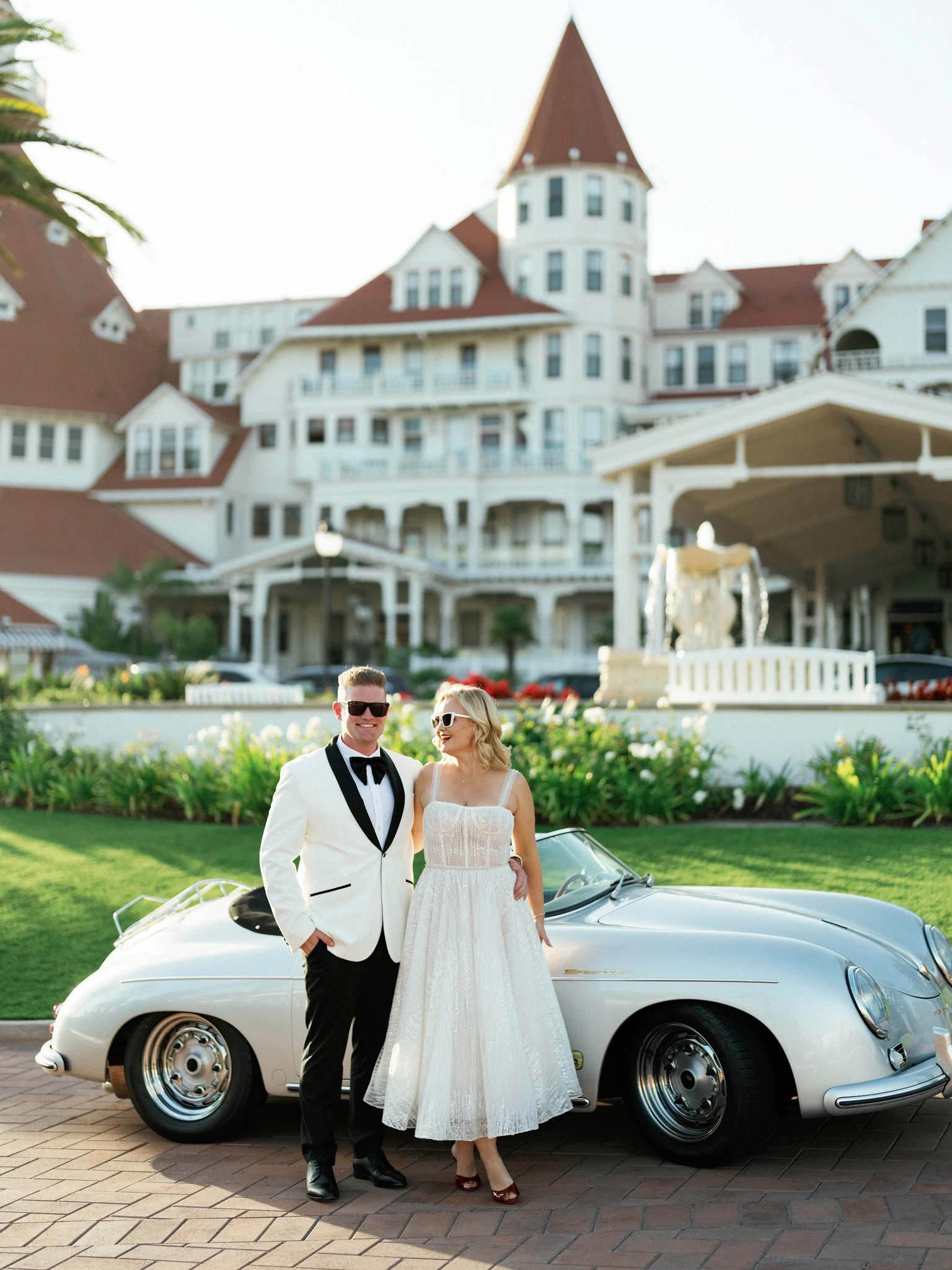 Bride and groom standing beside a white vintage car outside a historic hotel